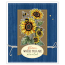 A handmade greeting card featuring a central illustration of yellow sunflowers, green leaves, and two bumblebees on a tan plaid background. The card has a blue wood-grain textured border with white stitched edges, twine bows on the sides, and an oval cream label at the bottom that reads 'Bloom WHERE YOU ARE planted'.