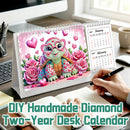 DIY handmade diamond two-year desk calendar shown on a desk with a person writing in a notebook. The calendar cover features a colorful diamond-look turtle surrounded by pink roses and hearts, with monthly calendar pages visible on the right side.