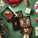 A set of Christmas-themed diamond painting canvases and a matching open canvas displayed on a green textured surface, surrounded by festive holiday props including pine branches, ornaments, a red ribbon spool, cinnamon sticks, and a small wrapped gift.