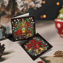 Two Christmas-themed diamond painting cards displayed on a tabletop. One card shows a golden lantern surrounded by red poinsettias, green leaves, snowflakes, and bells.