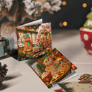 Two square Christmas greeting cards with detailed gingerbread-themed illustrations, displayed on a tabletop with festive background props including a red polka-dot cup and warm bokeh lights.