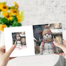 A person holds open a printed card or booklet showing two snowman illustrations: a small square version on the left page with the text 'Colorful World' and a larger detailed snowman scene on the right. The background is a softly blurred indoor setting with white brick wall and yellow flowers.