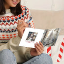 A person holding an open greeting card with a winter scene and the text 'Colorful World' in a cozy indoor setting. The person is wearing a patterned knit sweater and blue jeans.