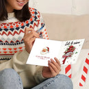 A person sitting indoors holds an open greeting card. The card shows a Santa illustration on one side and a snowman with the text 'Let it snow' on the other.