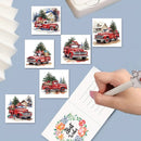 A hand writes in a floral 'Best Wishes' notepad while surrounded by small watercolor-style cards featuring red pickup trucks carrying Christmas trees. A white printer is partially visible at the top, and the scene is arranged on a light blue background.