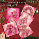 Six DIY diamond painting greeting cards with Christmas-themed designs, including a stocking, wreath, ornament, tree, mittens, and bow, arranged on a red background with holiday decorations. A hand with red nail polish is visible holding one card in the bottom left corner.