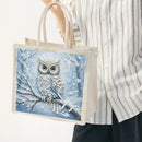 A person wearing a white and gray striped button-up shirt holds a clear plastic tote bag with a winter owl design. The bag has a light blue background with a detailed owl and snowflake pattern, white handles, and a beige inner lining visible at the edges.