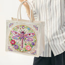 A person wearing a white and gray striped button-up shirt holds a clear vinyl tote bag decorated with a large colorful embroidered dragonfly and floral motifs on the front.