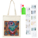 An off-white canvas tote bag with a colorful, highly detailed owl diamond painting design on the front, shown alongside its included accessories: a green paint pot, pink and red paintbrushes, and several clear plastic packets of diamond painting beads.