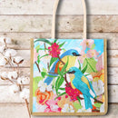 A canvas tote bag with a colorful diamond painting design of bluebirds and flowers, displayed on a rustic white wood background next to cotton bolls.