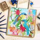 A canvas diamond painting kit featuring a design of two blue birds perched on a flowering branch. The kit is displayed in a styled flat-lay arrangement on a white lace background with decorative props including pencils, a small gift box, and miniature frames.