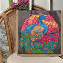 A tote bag with a colorful diamond painting or bead art design of a peacock and flowers, resting on a woven rattan chair with flowers in the background.