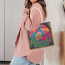 A woman wearing a pink corduroy cardigan and light blue jeans carries a canvas tote bag with a colorful beaded peacock design on a dark gray background.