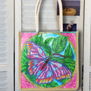 A canvas tote bag with cream-colored handles, featuring a colorful beaded-style butterfly design on a pink background with green leaves and the words 'Wander Well'.