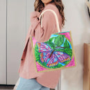 A woman wearing a pink cardigan and light blue jeans carries a colorful tote bag with a glittery butterfly design on a pink background. The bag has cream-colored shoulder straps and is shown in an indoor setting.