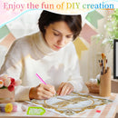 A woman in a cream turtleneck sweater is shown in a brightly lit room, carefully applying adhesive diamond painting or beadwork onto a circular patterned sheet with a pink-handled tool. The scene includes craft supplies like paintbrushes, small decorative items, and a pastel banner in the background, with a text overlay at the top reading 'Enjoy the fun of DIYY creation'.