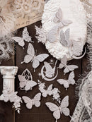 A collection of white paper cutouts featuring butterflies, roses, stars, and vintage architectural details, arranged on a dark wood background with decorative lace and a round floral embellishment.