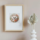 A framed art print featuring a cute hedgehog surrounded by orange flowers, displayed on a beige wall next to a white decorative vase with dried palm leaves.
