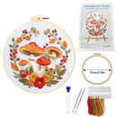 Embroidery DIY Art Kit shown with a completed circular embroidery hoop featuring red-and-white mushrooms, orange flowers, and green leaves on a white fabric background. The kit also includes a package card labeled 'Embroidery DIY Art Kit,' a second empty hoop marked 15cm/5.