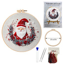 Christmas-themed embroidery kit shown on a white background, including a completed circular embroidery piece with Santa in a wreath, the product packaging, an empty hoop, measurement callout, needles, thread, and a small tube.