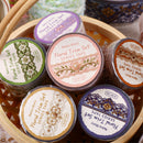 Collection of floral trim sets in small containers with decorative labels on a wooden surface.