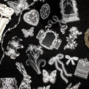A flat lay of clear acrylic or glass craft stamps featuring lace and filigree designs, including butterflies, lilies, ribbons, hearts, and frames, arranged on a black textured background.
