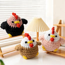 Three crocheted chicken toys in different colors on a wooden surface with a lamp in the background.