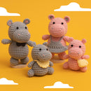 Four crocheted hippo plush toys in different sizes and colors, including gray and pink tones, displayed on a bright yellow background with white cloud cutouts.