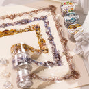 Several rolls of decorative washi tape with ornate floral and lace-like patterns are arranged on a light surface. The tape features gold, purple, blue, and brown designs, and some rolls are partially opened to show the patterned strips.