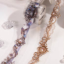 Two decorative patterned rolls of washi tape displayed on a clean white background. One roll features an iridescent silver and blue filigree design with faux pearls, and the other shows a warm gold-toned lace and scroll pattern.