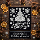 A square black Christmas art print featuring a white lace-style tree, snowflakes, and the words 'Merry Christmas,' styled on a dark wood surface with dried orange slices, pinecones, and warm fairy lights. A banner at the bottom reads 'Create Warm Holiday Memories.