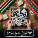 A gift box wrapped in black and white ornate paper with a silver ribbon and bow, held by two hands over a wooden table decorated with wrapping paper, scissors, pine branches, and gift tags. A dark banner at the bottom reads 'Ready to Gift'.