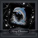 A rhinestone-style dolphin design on a black square panel, surrounded by silver and blue decorative pearls and ornaments on a dark draped fabric background. A banner at the bottom reads “Merry Christmas.