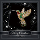 A large, ornate Christmas-themed brooch shaped like a hummingbird, crafted with gold, green, red, and white rhinestones. It is displayed on a black satin background with decorative silver pearl-like accents and a 'Merry Christmas' banner at the bottom.