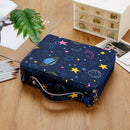 A navy blue zippered pouch with a colorful space-themed print of planets, stars, and moons, styled on a wooden desk with pencils, a green leaf, and stationery.
