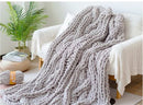 Gray chunky knit blanket draped over a white sofa in a cozy living room.