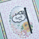 A close-up of a handmade greeting card featuring a scalloped white border with pink floral dots, a clear window, sequins, and a black decorative sign that reads 'thank you' over a floral background.