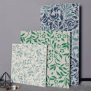 Four decorative wall panels with floral and scroll damask patterns in blue, green, and gray tones, arranged against a gray wall with small decorative props on the floor.
