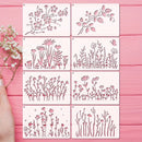 Six square metal stencils with pink floral and botanical cutout designs arranged in a 3x2 grid on a pink wooden surface, with a hand holding baby's breath flowers at the left edge.