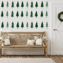 Green pine tree wall decals arranged in three rows on a white wall above a wooden bench with floral throw pillows in a bright room.