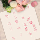 A flat-lay view of a white sheet of paper printed with various pink floral and geometric stencils, styled with pink roses and a green flower stem at the top edge.