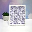 A square white card or art print featuring an ornate purple damask floral pattern, displayed on a white surface with a small potted succulent and a soft purple-blue bokeh background.