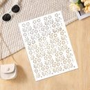 A white rectangular sheet with an allover laser-cut floral and leaf pattern, photographed on a light wood surface with a woven textile, sunglasses, a small purse, and flowers as styled props.
