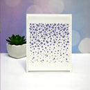 A white square art print or card featuring a pattern of purple dots of varying sizes, displayed on a white surface with a small potted succulent and a pastel purple and blue bokeh background.