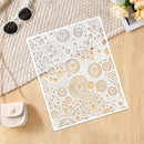 A white laser-cut decorative panel with intricate circular and radial cutout patterns, styled on a light wood surface with a textured cream fabric, sunglasses, a small purse, and flowers.