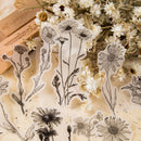 Clear acrylic stamp designs featuring black ink botanical illustrations of daisies and wildflowers, arranged on a light beige textured surface with dried white flowers and a wooden block in the background.