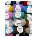 A close-up arrangement of multiple Poppy Crafts yarn skeins in assorted colors, including blue, purple, red, yellow, pink, teal, green, gray, brown, and cream, each with a white paper label.