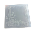 A square translucent plastic mold or stamp with an embossed floral design featuring a rose and leaves in the bottom-left corner, set against a plain white background.