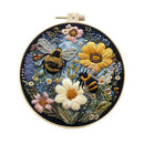 A circular embroidered floral and bee artwork displayed in a wooden embroidery hoop against a plain white background. The design features two bumblebees among large white and yellow flowers, pink blossoms, blue and purple flowers, and green leaves on a dark blue ground.