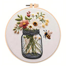 Embroidered floral art in a circular wooden hoop, featuring a mason jar filled with white, pink, and yellow flowers, green stems, and a small embroidered bee on a white background.